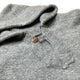 A gray woolen sweater lies flat, showcasing a single brown button on its folded collar, highlighting its soft, textured surface in a neutral setting.