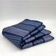 Chimborazo baby alpaca wool blanket – a folded, blue, striped blanket rests neatly on a plain white surface, its soft fabric creating gentle curves and shadows
