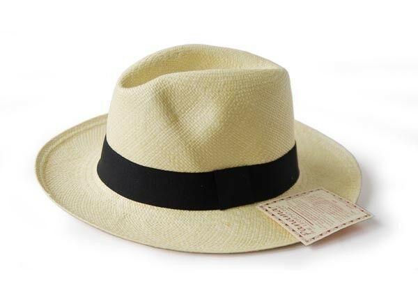 A straw hat rests on a surface, featuring a wide black band. A small tag with fine print is attached to the band, offering a simple, classic look.