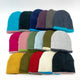 A collection of beanies in various colors, including blue, green, red, and gray, are neatly arranged on a plain white surface. Each beanie features a contrasting brim.