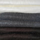 Pilahuin baby alpaca wool blanket – stacked fabrics in a horizontal arrangement: white, gray, and dark brown woolen textures, layered neatly, showcasing their thickness and softness in a close-up view