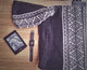A black and white patterned knit sweater lies on a wooden surface beside a Kindle displaying text and a digital watch showing 12:22.
