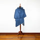 A blue shawl draped over a dress form stands on a wooden floor against a plain white wall background.