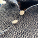 A textured blue garment features two white circular buttons; they are fixed on a knitted fabric, with a partially raised collar in a softly-lit environment.
