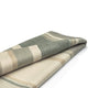 Deleg baby alpaca wool blanket – a folded, striped blanket with green, beige, and cream horizontal stripes is lying on a smooth, white surface