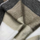 Mogato baby alpaca wool blanket – a soft, multicolored wool fabric lays gently folded, featuring alternating gray, tan, and cream stripes with a woven texture, creating a cozy, textured appearance