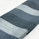 Toacazo baby alpaca wool blanket – a folded, striped fabric in varying shades of gray rests on a white surface. The texture appears soft and woolly, suggesting warmth and comfort. No text is present