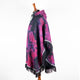 A tie-dye patterned poncho with pink and black hues drapes over a mannequin. It features a hood and fringed edges. The background is a plain white setting.