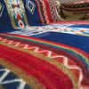 A colorful, intricately-patterned blanket featuring geometric designs lies flat, displaying vivid hues of blue, red, and gold, set within an interior space.