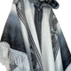 Palora lightweight alpaca wool hooded poncho – a woolen poncho hangs against a plain background, featuring a black and white geometric pattern, fringed edges, and a buttoned collar for closure