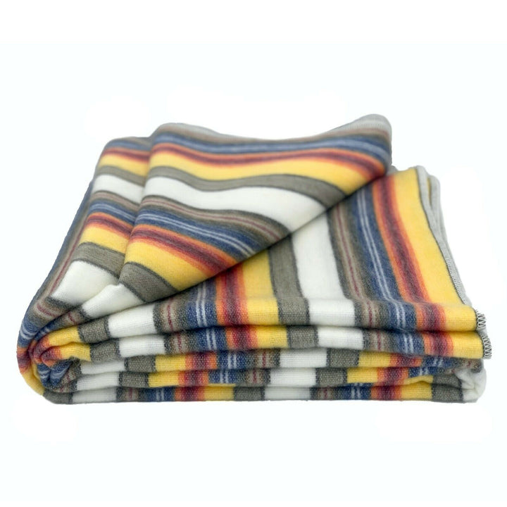 Guayan baby alpaca wool blanket – a folded blanket displays colorful horizontal stripes in shades of yellow, blue, red, and gray on a white background, situated against a plain white backdrop