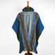 A blue poncho with intricate orange and white geometric patterns drapes over a mannequin, set against a plain, light-colored background.