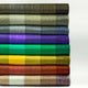 Yatzaputzan baby alpaca wool blanket – colorful fabrics are neatly stacked in a horizontal pile, each layer showcasing a different shade, including earthy tones and vibrant bright colors, against a plain background