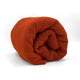 A rolled-up, orange blanket or fabric lies on a white background, appearing soft and textured, with no visible text or additional objects surrounding it.