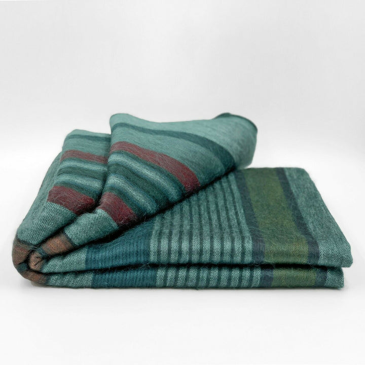 Pallalanga baby alpaca wool blanket – a folded blanket with green, blue, and red stripes rests neatly on a plain, light background. The texture appears soft and woven