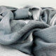 Toacazo baby alpaca wool blanket – soft, gray fabric drapes in loose, gentle folds, creating a textured and inviting surface. It spreads across a neutral backdrop, emphasizing its plush and cozy appearance
