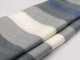 Poguios baby alpaca wool blanket – a folded blanket displays wide horizontal stripes in shades of gray, cream, and blue, resting on a plain light-colored surface