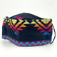 Cloth face mask featuring vibrant geometric pattern with triangles in red, blue, yellow, and orange. It rests against a plain white background, highlighting the colorful design.
