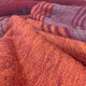 Pallatanga baby alpaca wool blanket – a close-up of soft, folded, red and orange wool fabric with alternating striped and solid textures, creating a warm, textured pattern