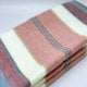 Rucu baby alpaca wool blanket – a folded fabric with horizontal stripes in peach, white, gray, and yellow hues rests on a plain white surface, showcasing its soft texture and pattern