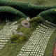 Wool fabric with a herringbone pattern features three textured buttons. The material is green with beige accents, creating a rustic appearance in cozy, woven surroundings.