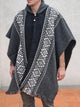 A person wears a gray, patterned poncho with white geometric designs, standing in a tiled area with a neutral background.