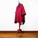 A red hooded cape with black trim displayed on a mannequin stands in a room with a wooden floor and white walls.