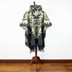 Tarqui alpaca wool hooded poncho – poncho displayed on a mannequin stand, featuring a black and cream geometric pattern with fringed edges. It is set against a white wall and wooden floor background
