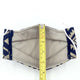 A fabric face mask with blue geometric patterns lies flat. A measuring tape, marked with yellow and black numbers, is vertically placed on the mask, displaying a measurement slightly above 4 inches.