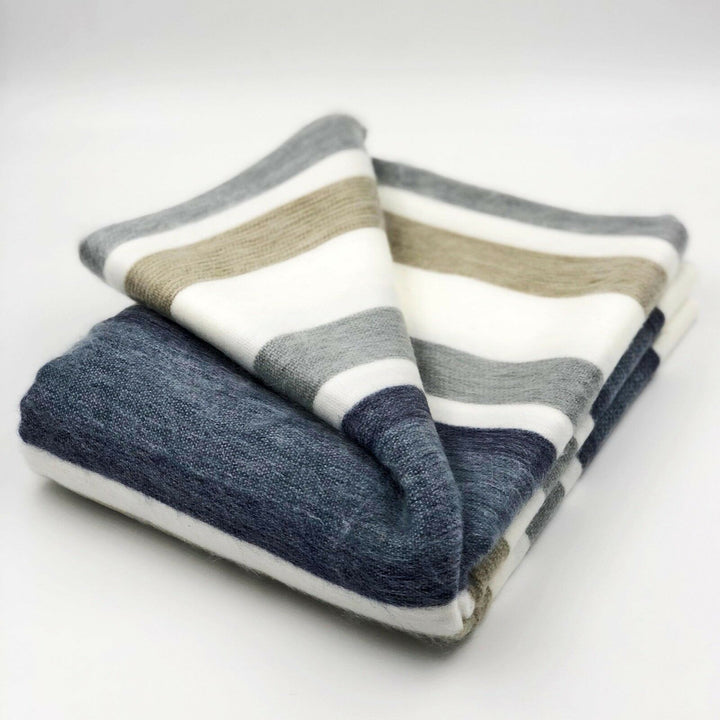Pilishurco baby alpaca wool blanket – a folded, striped wool blanket with gray, white, and beige stripes lies on a plain white surface, displaying soft texture and neatly arranged layers