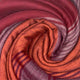 Pallatanga baby alpaca wool blanket – a colorful blanket is tightly coiled, displaying shades of orange, red, and purple with striped patterns. The fabric appears soft and textured, filling the frame. There is no text