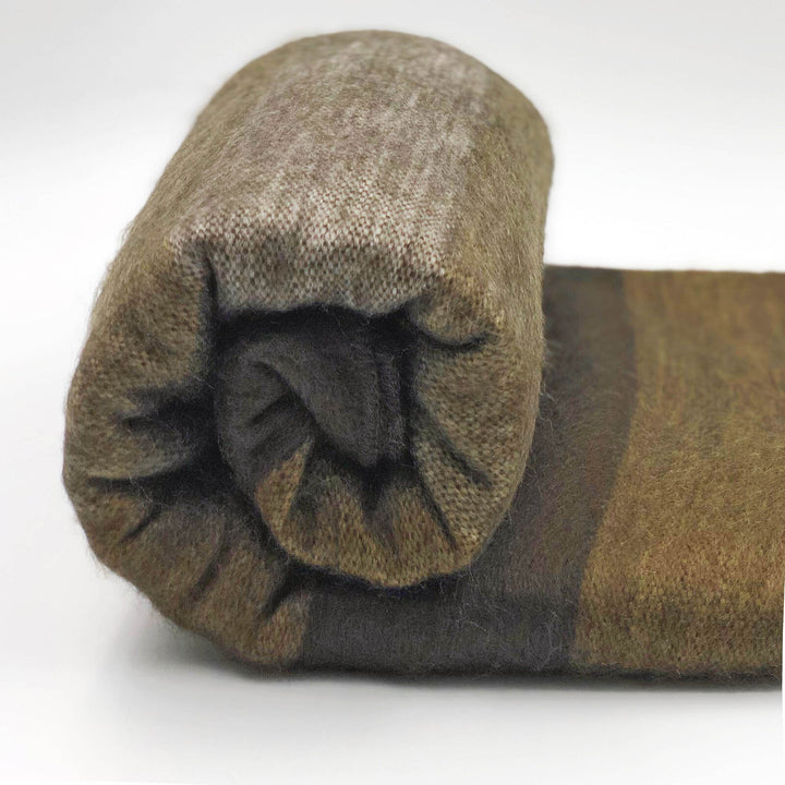 Alpaca wool queen blanket – a rolled-up brown wool blanket sits on a flat surface. The blanket features gradient shading, accentuating its texture in a well-lit environment
