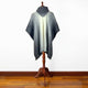 Zuleta llama wool hooded poncho – a gray and white knitted poncho drapes over a wooden stand, displayed in a room with wooden floors and a plain white wall backdrop