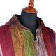 A multicolored striped woolen garment with a wooden button fastening displayed on a black mannequin torso, set against a plain white background.