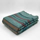 Pallalanga baby alpaca wool blanket – a folded, striped blanket with green, brown, and red colors rests on a plain white surface, emphasizing its soft texture and neatly arranged layers