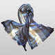 A blue and white striped scarf is arranged with flowing ends and a central loop, showcasing its soft texture and fringed edges, set against a plain light background.