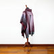 A maroon and gray scarf drapes elegantly over a wooden mannequin stand, set against a simple white wall and wooden floor.