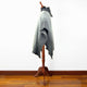 Zuleta llama wool hooded poncho – a gray wool poncho drapes over a wooden mannequin stand, positioned on a polished hardwood floor against a plain white wall