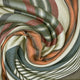 Suropata baby alpaca wool blanket – a soft, multi-colored, striped fabric in shades of green, orange, and cream is intricately swirled, creating a spiral pattern. The texture appears smooth and cozy