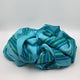 Machay baby alpaca wool blanket – a crumpled fabric with blue, teal, and green stripes rests on a flat, white surface, creating a textured and colorful pile