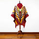 Guismi alpaca wool hooded poncho – a colorful poncho displayed on a wooden mannequin stand. Featuring intricate geometric patterns in red, yellow, and green, the poncho is set against a plain white wall and wooden floor