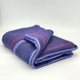 Punguloma baby alpaca wool blanket – a folded, purple wool blanket with red and pink stripes rests on a plain, light surface
