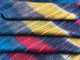 Alpaca wool queen blanket – folded, multicolored woven fabric lying flat, showcasing vibrant diagonal stripes of blue, red, yellow, and green hues. The texture appears soft and plush, suggesting cozy material