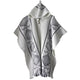 A white wool poncho with a hood features black geometric patterns and a central button fastening, displayed against a plain white background.
