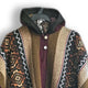 A knitted sweater hangs on a hanger, featuring a hood and displaying intricate geometric patterns in brown, beige, and maroon, with two white buttons on the front.