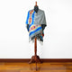 A colorful shawl with geometric patterns draped over a mannequin, standing on a polished wooden floor against a plain white background.