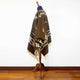 Clint Eastwood alpaca wool poncho – a brown wool poncho with geometric and floral patterns drapes over a mannequin stand. The room has a wooden floor and a plain white wall, providing a minimalist background