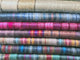 Wholesale lot of 10 queen alpaca wool blankets – stacked woolen blankets display colorful stripes, showcasing a gradient from neutral to vibrant hues, arranged neatly. The textures appear soft and slightly fuzzy, suggesting warmth and coziness