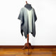 Zuleta llama wool hooded poncho – a gray knitted poncho drapes over a wooden mannequin stand, displayed against a plain white wall on a wooden floor