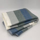 Poguios baby alpaca wool blanket – a folded blanket features wide horizontal stripes in shades of blue, gray, and white, resting on a plain white background